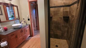 A bathroom with a wooden vanity, a large mirror, a sink, and a shower area with tiled walls.