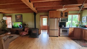 Ein gemütliches Wohnzimmer mit Kamin, Holzboden und einem Essbereich, im Hintergrund ist eine Küche zu sehen.