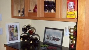 A kitchen with wooden cabinets, a black countertop, and various items like wine bottles, a framed picture, and a box of dog biscuits. - 1600 Sq Ft Craftsman Cottage in the Country (Sequim)