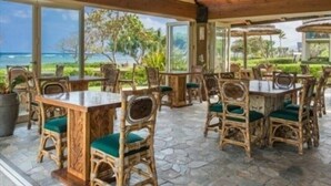 Un espace de restauration en plein air, doté de mobilier en osier et d’un sol en pierre, offrant une vue panoramique sur l’océan.