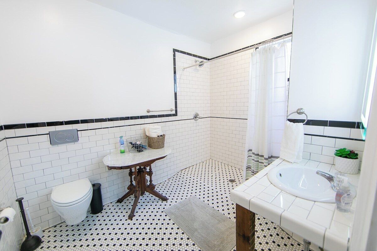 A bathroom with a white toilet, a sink with a mirror, a shower area, and a patterned floor.