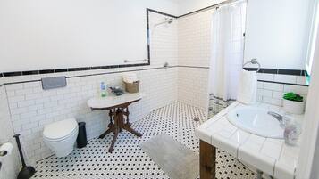A bathroom with a white toilet, a sink with a mirror, a shower area, and a patterned floor.
