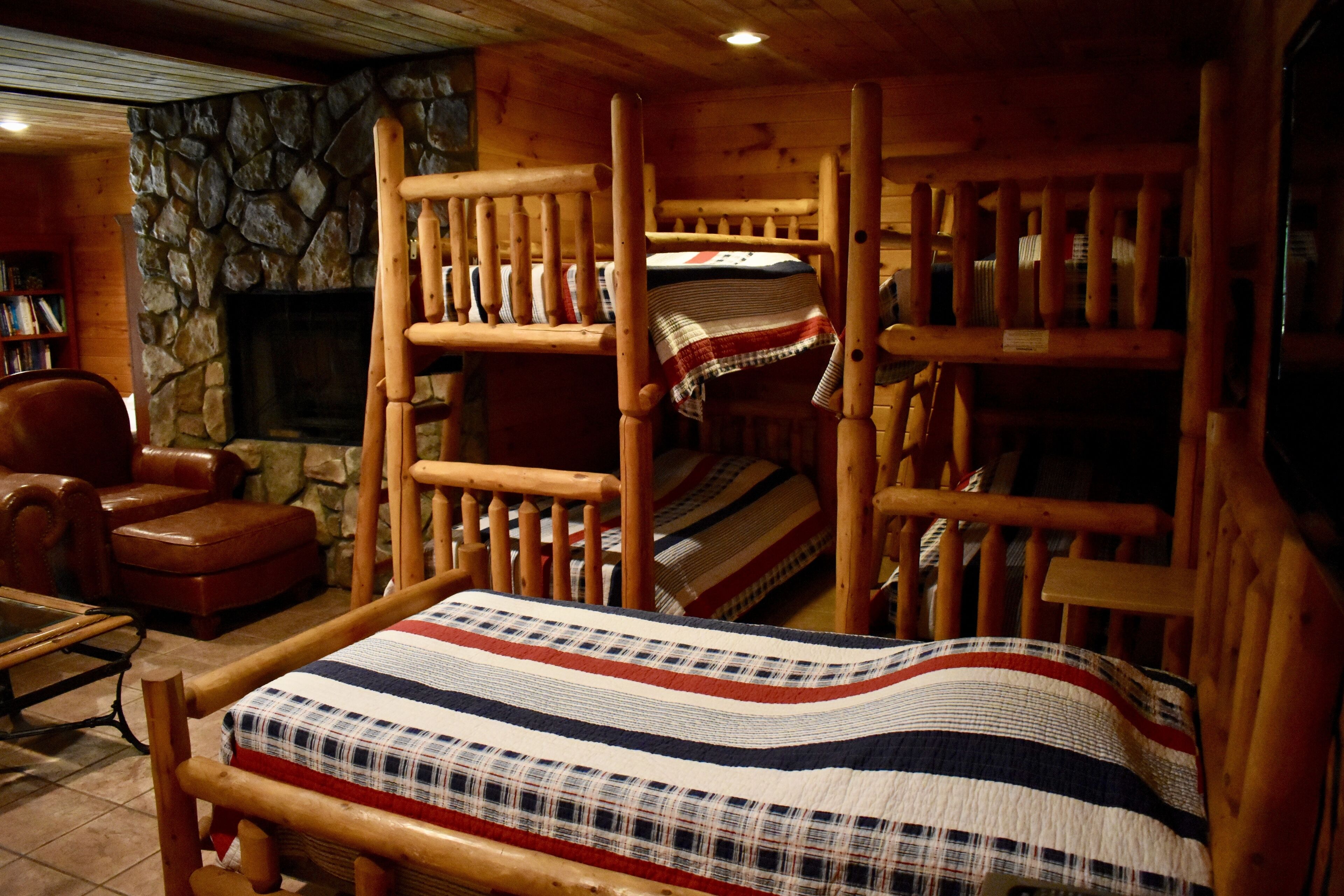 A cozy cabin-style room with a bunk bed, a wooden chair, a fireplace, and a stone wall.
