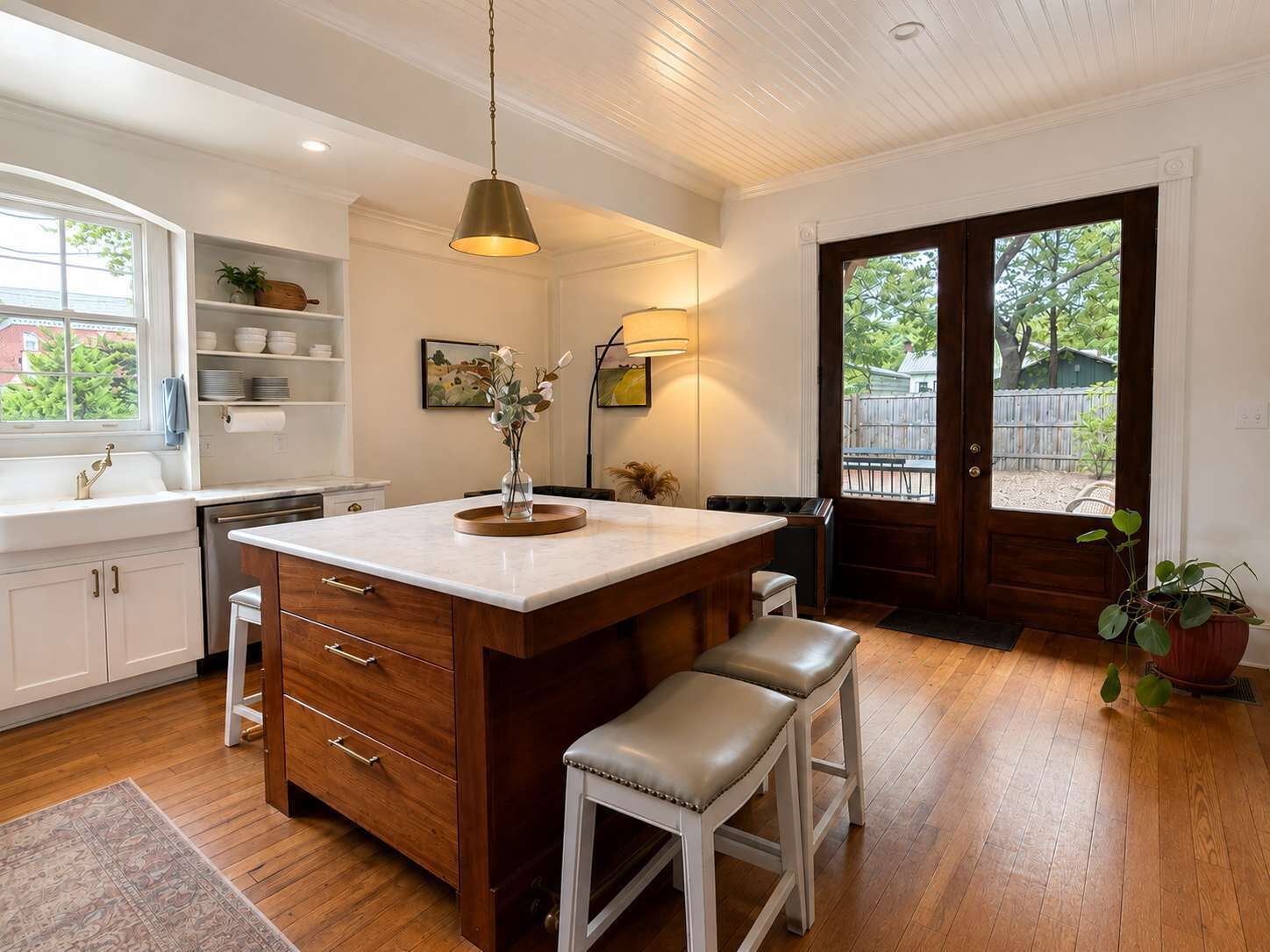 A kitchen with a central island, wooden cabinets, a sink, and a dining area with stools.
