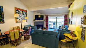 A living room with a fireplace, a television, a dining table with chairs, and a balcony with a view. - Spacious Condo w/ FREE WiFi, Parking, Heated Pool, Hot Tubs, Skier Shuttles (Avon)