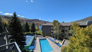 A pool area with blue chairs and a tennis court, surrounded by trees and buildings. - Spacious Condo w/ FREE WiFi, Parking, Heated Pool, Hot Tubs, Skier Shuttles (Avon)
