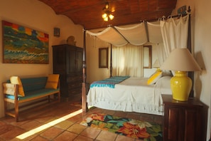 A bedroom with a bed, a bench, a lamp, and a painting on the wall.