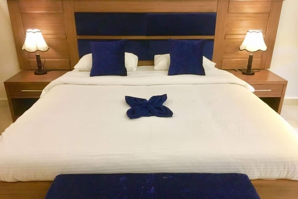 A neatly made bed with a white duvet and blue pillows, a blue decorative pillow on the bed, and two bedside lamps on wooden nightstands.
