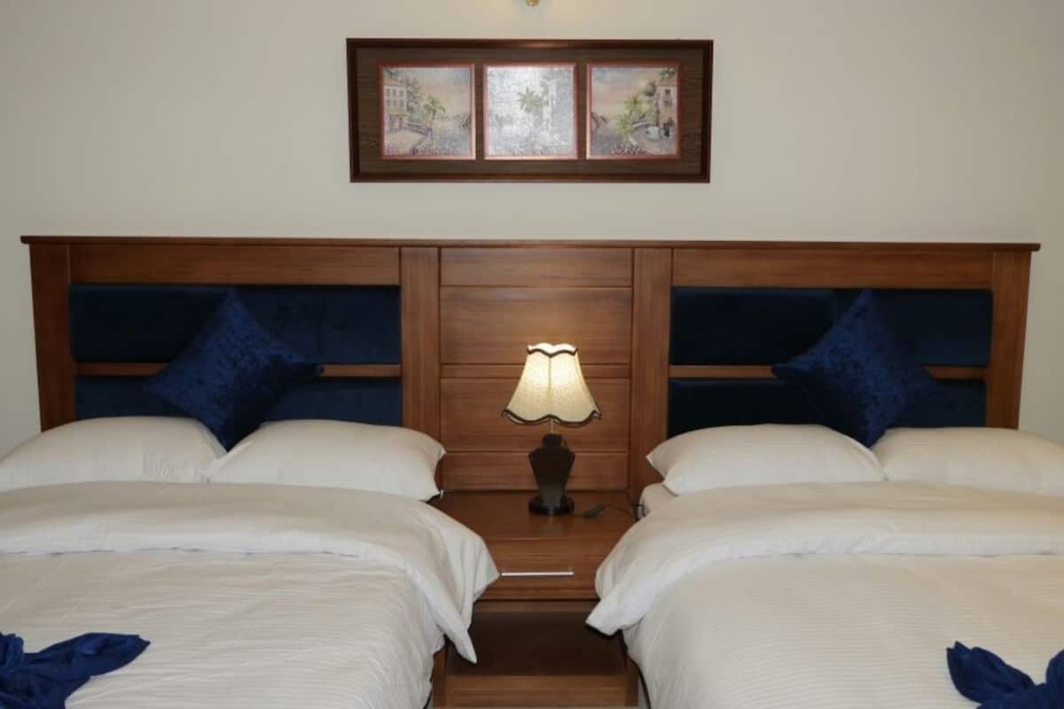 A hotel room with two beds, a nightstand with a lamp, and a framed picture above the beds.