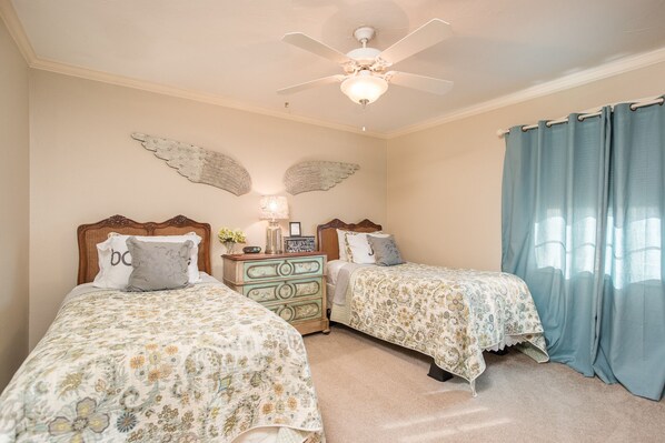 A bedroom with two beds, a ceiling fan, decorative wall art, and a window with curtains.