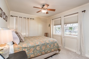 A bedroom with a bed, a ceiling fan, a window with curtains, and a nightstand with a lamp.