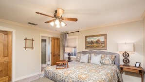 A bedroom with a bed, a bench, a ceiling fan, a painting, and a nightstand. - Walk To Main. Hill Country Stone Haus With Unique Outdoor Pavillion (Fredericksburg)