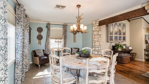 A dining area with a round table and six chairs, a chandelier, and a stone wall. - Walk To Main. Hill Country Stone Haus With Unique Outdoor Pavillion (Fredericksburg)
