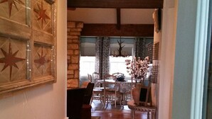 A hallway with a patterned rug, wooden flooring, and a dining area with chairs and a table. - Walk To Main. Hill Country Stone Haus With Unique Outdoor Pavillion (Fredericksburg)