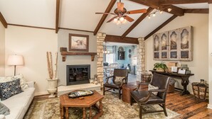 A cozy living room with a fireplace, wooden furniture, and a stone wall. - Walk To Main. Hill Country Stone Haus With Unique Outdoor Pavillion (Fredericksburg)