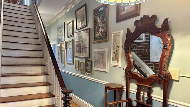 A staircase with a wooden handrail and a wooden chair with a mirror on the wall.