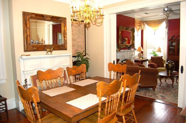 A dining room with a wooden table and chairs, a chandelier, and a large mirror on the wall.