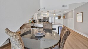 A modern kitchen with white cabinetry, stainless steel appliances, and a dining area with wicker chairs and a glass table. - Stunning Oceanfront on Crystal Beach with 2 King beds. Beach service included. (Destin)