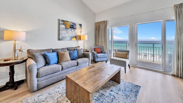A modern living room with a grey sofa, a wooden coffee table, and a view of the ocean through large sliding doors. - Stunning Oceanfront on Crystal Beach with 2 King beds. Beach service included. (Destin)