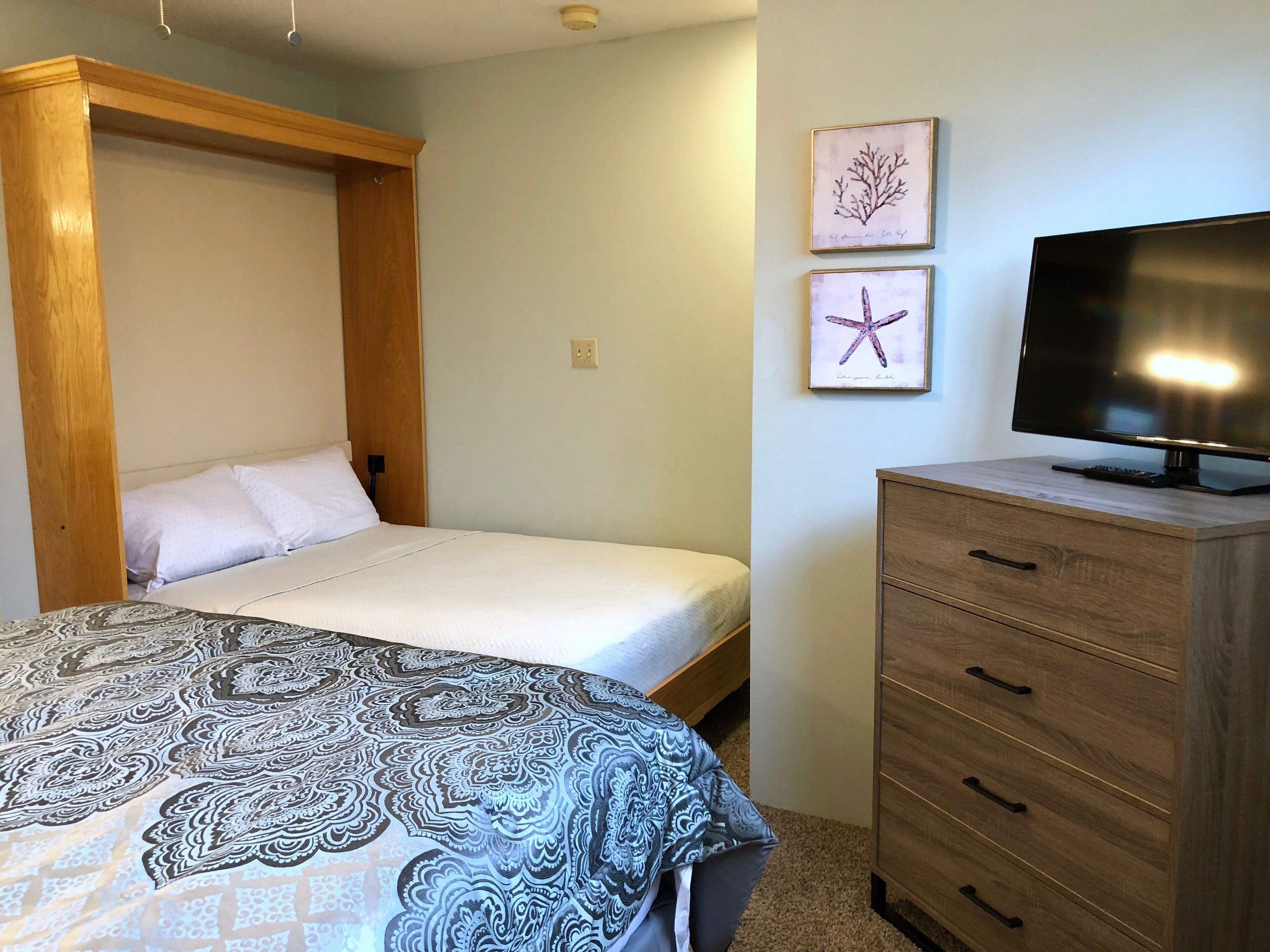 Een slaapkamer met een bed, een televisie op een houten kast en twee ingelijste foto’s aan de muur.