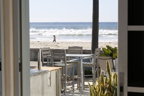 Un espace extérieur aménagé avec des tables et des chaises, offrant une vue sur une plage avec des vagues et une personne qui se promène.