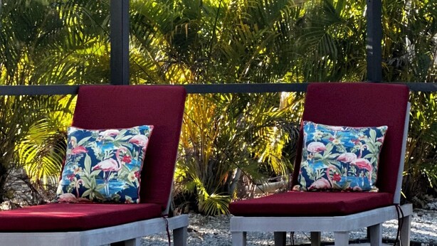 A covered outdoor seating area with two red cushioned chairs and floral-patterned cushions. - Quick Walk To Beach, Restaurants, Shops, Movies. Updated, Spacious. Private Pool (Marco Island)