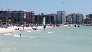 A beach with people, umbrellas, and buildings in the background. - Quick Walk To Beach, Restaurants, Shops, Movies. Updated, Spacious. Private Pool (Marco Island)
