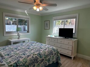 Une chambre à coucher avec un lit, une commode, une télévision et des fenêtres.