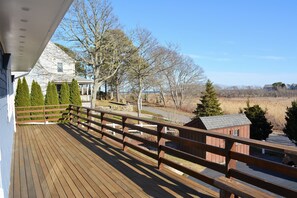 A wooden deck with a railing, overlooking a residential area with houses and trees.