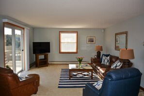 A living room with a television, a coffee table with a vase of flowers, a sofa, and a chair.