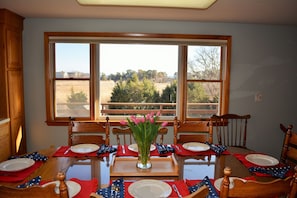 A dining table set for six with red placemats, white plates, and a vase of pink tulips.