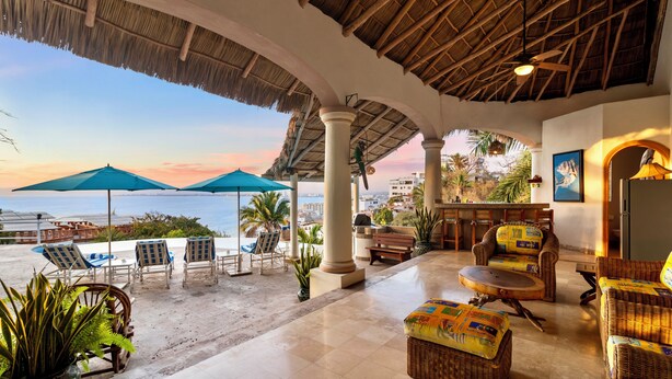 A beachside lounge with wicker furniture, a pool, and umbrellas.