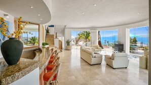 A spacious living area with a large window overlooking the ocean, a kitchen with a granite countertop, and a seating area with a white sofa and chairs.