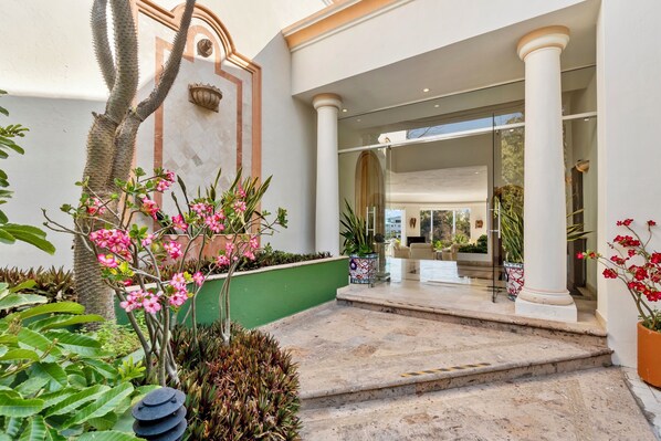 Entrada de hotel con una escalera de mármol, columnas y plantas en macetas.