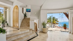 A modern interior with a staircase leading to a balcony overlooking the sea.
