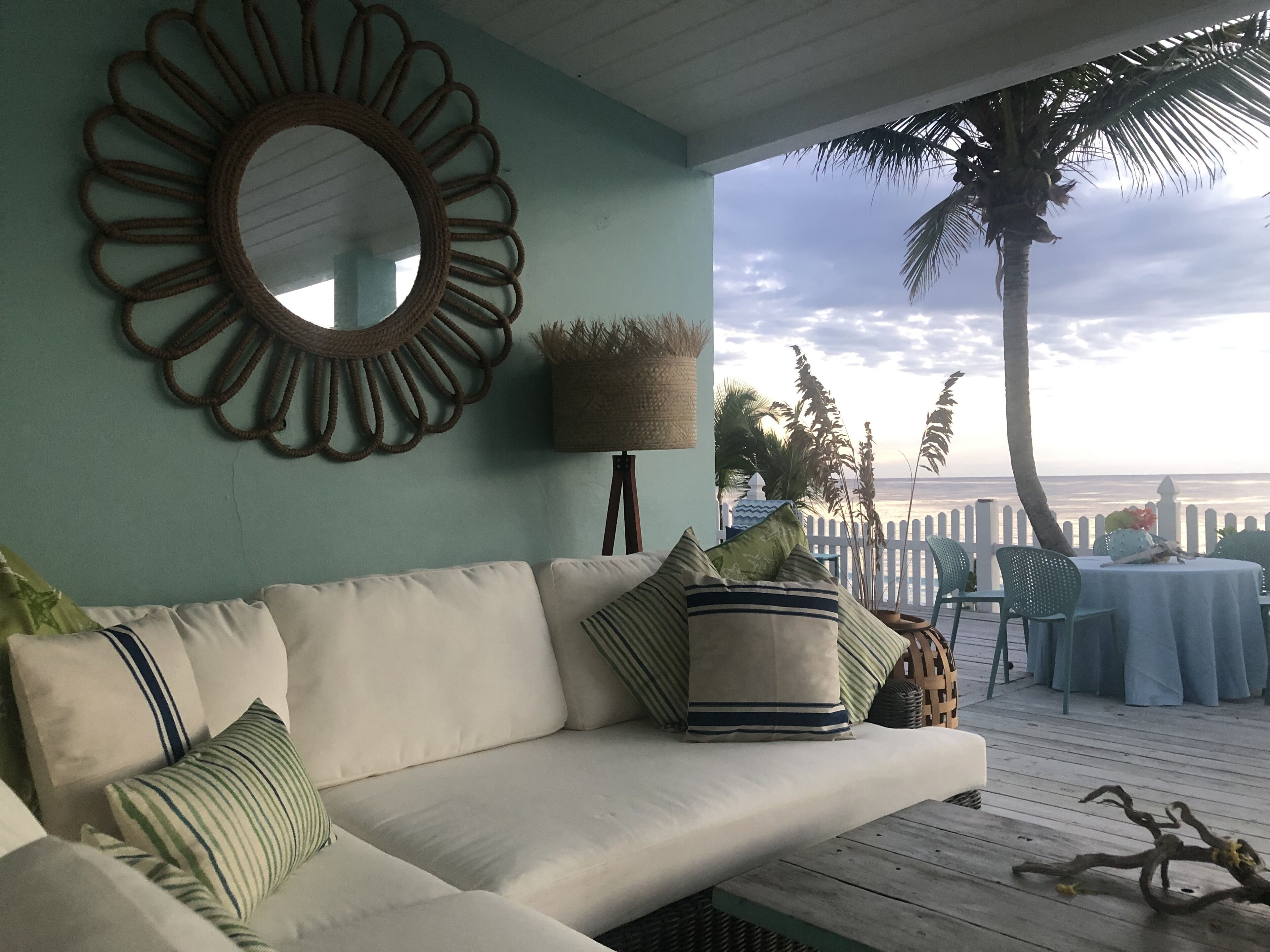 A cozy outdoor seating area with a cushioned sofa, a round mirror, and a table set for dining.