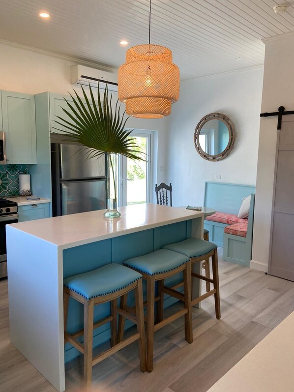 Cozinha moderna com ilha central, banquetas de madeira, luminária pendente e vista para o exterior.