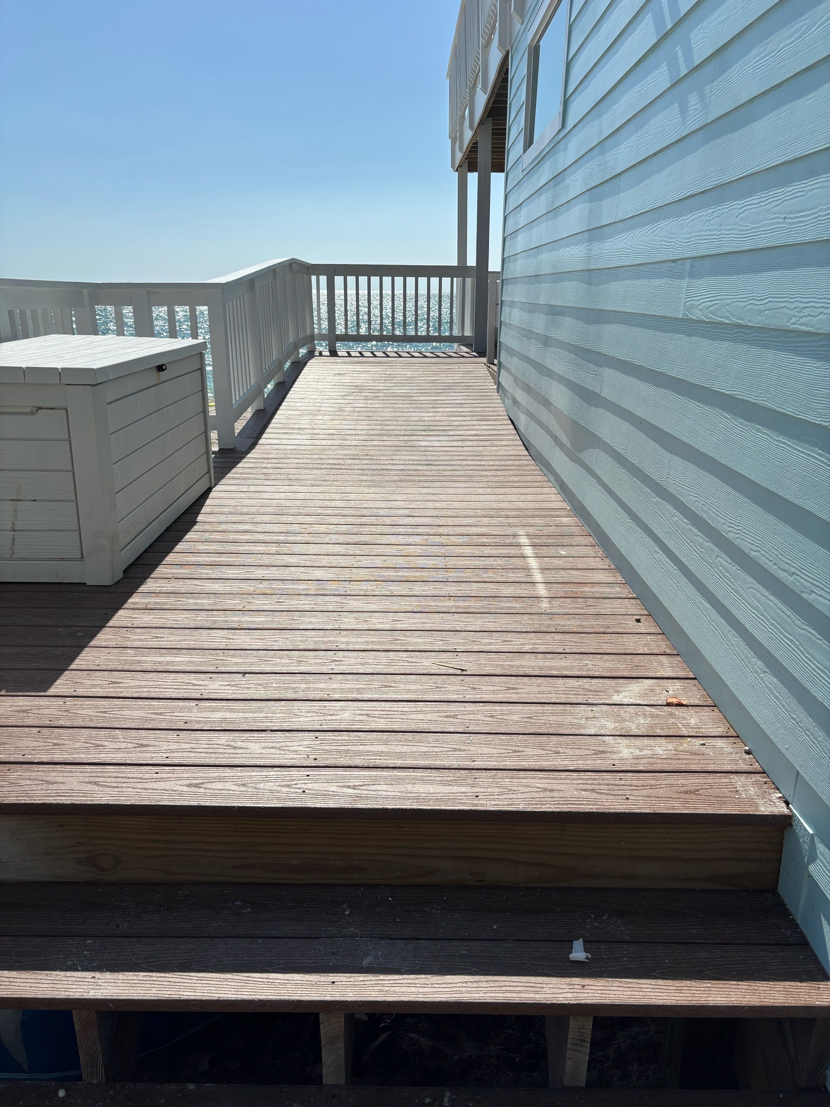 A wooden deck with a white railing, leading to a building with a light blue exterior.