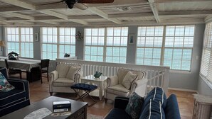 Een ruime woonkamer met een groot raam met uitzicht op de zee, ingericht met een bank, stoelen en een salontafel.