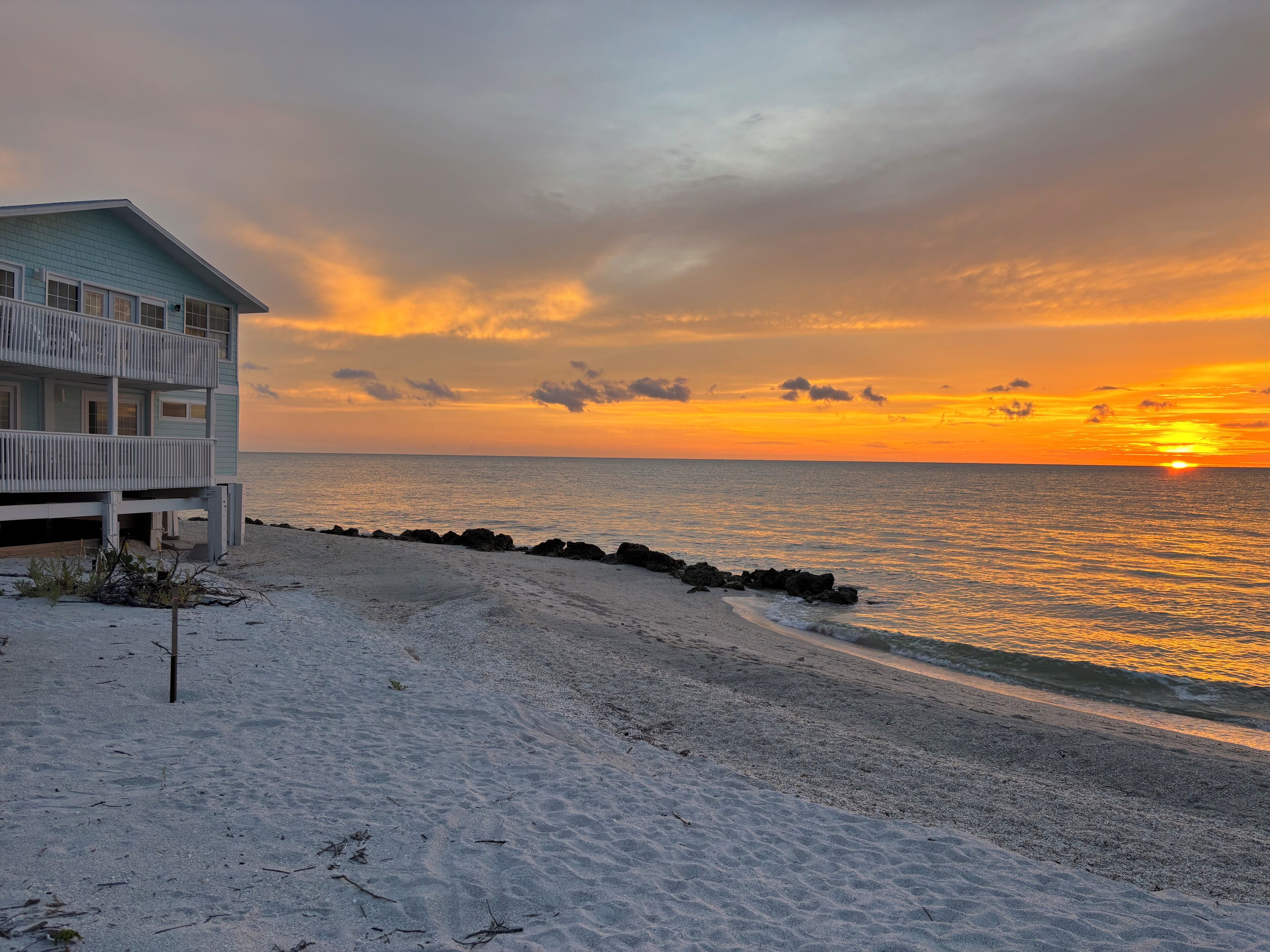 Ein Strandhaus mit Balkon mit Blick auf den Ozean bei Sonnenuntergang.