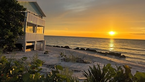 Una propiedad frente a la playa con un edificio de dos pisos, un balcón y vista al océano al atardecer.