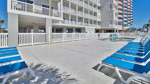 Ein Hotel mit mehreren Balkonen, einem Poolbereich mit Liegestühlen und wolkenlosem, blauem Himmel.