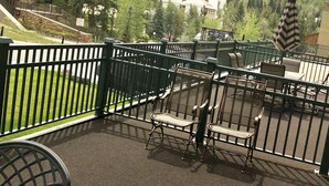A balcony with outdoor seating, a stone building, and a view of a forested valley.