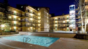 A multi-story hotel with a swimming pool, outdoor lighting, and a brick pathway.