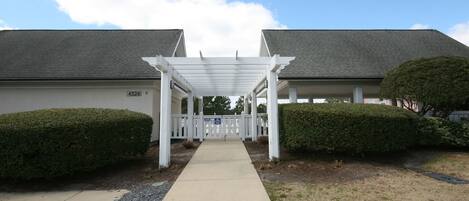 A covered walkway leading to a building with a number 4524 sign, flanked by neatly trimmed hedges.