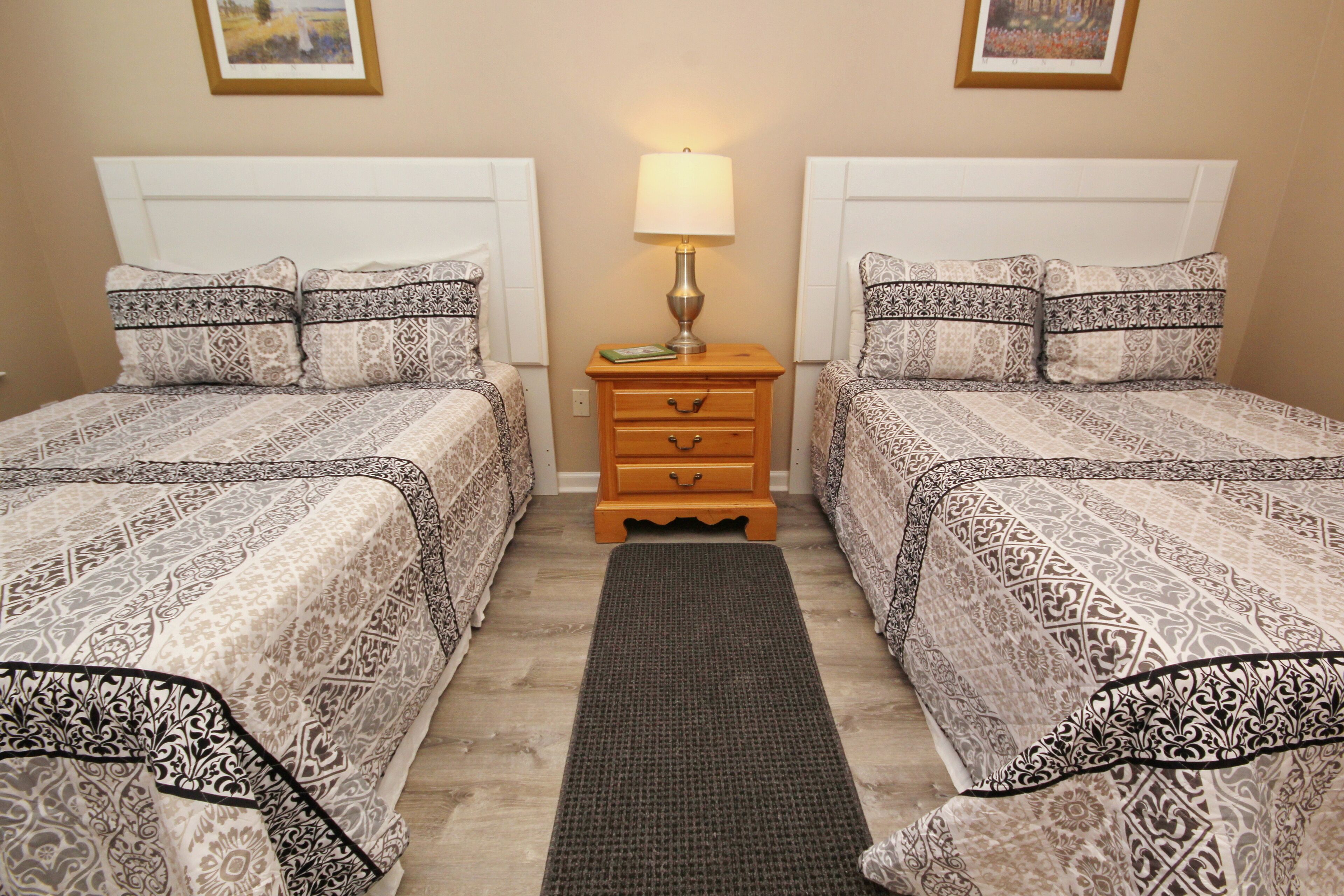 A hotel room with two beds, a nightstand with a lamp, and a rug.