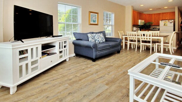A living room with a flat-screen TV, a grey sofa, a coffee table, and a dining area with a white table and chairs. - Legends Golf Resort - 2 Bedroom on ground floor, Wi-Fi included (Myrtle Beach)