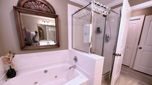 Ein Badezimmer mit einer großen Badewanne, einer Duschkabine und einem Spiegel mit dekorativem Rahmen.