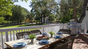 Un área de comedor al aire libre con una mesa de madera dispuesta para seis personas, rodeada de sillas de mimbre.