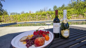 Un montaje para picnic con una fuente de fruta, queso y pan, y dos botellas de vino en un banco junto a una piscina.